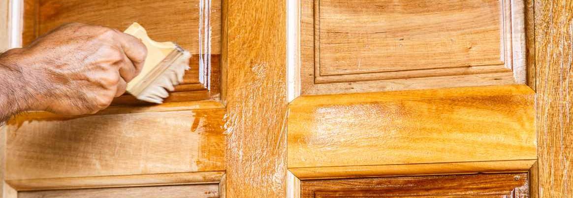 Person lasiert eine Tür mit einem Pinsel.